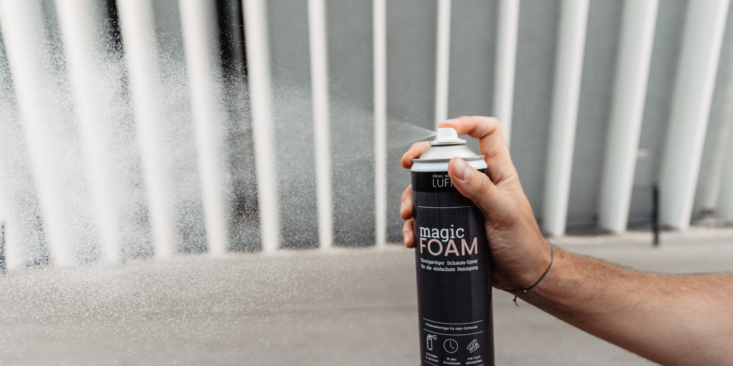 Eine Hand hält eine Magic Foam Dose, während das Produkt auf eine Oberfläche gesprüht wird. Die Nutzung des Schaumreinigers wird veranschaulicht, während er auf eine Oberfläche aufgetragen wird.